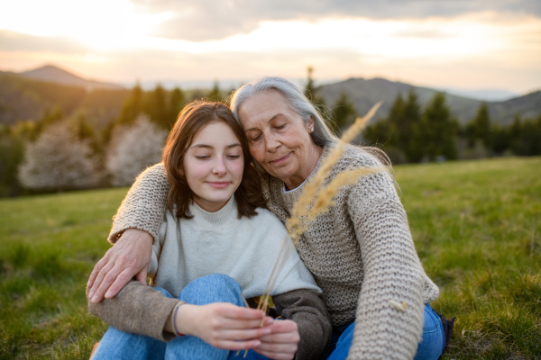 A happy senior grandmother with teenage granddaguhter hugging in nature on spring day.