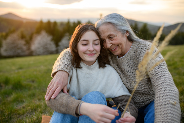 A happy senior grandmother with teenage granddaguhter hugging in nature on spring day.