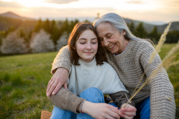 A happy senior grandmother with teenage granddaguhter hugging in nature on spring day.