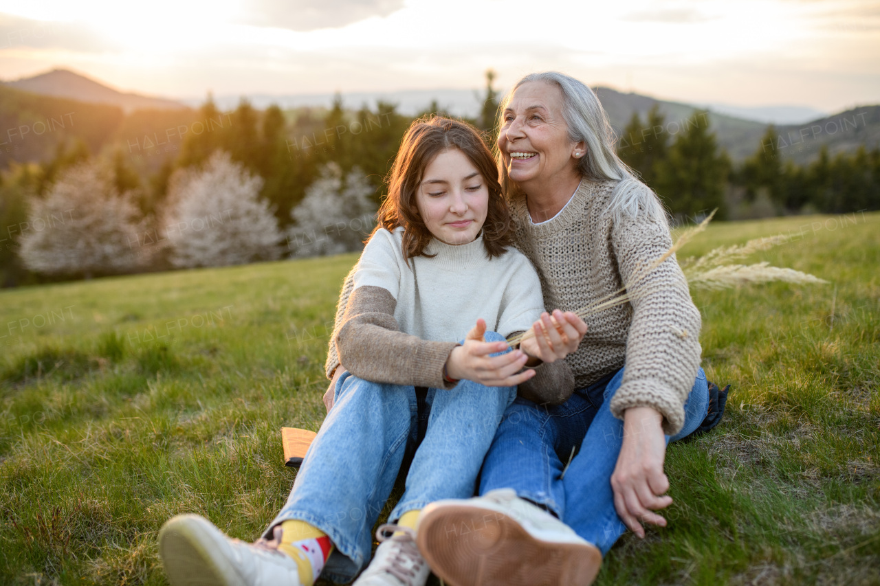 A happy senior grandmother with teenage granddaguhter hugging in nature on spring day.