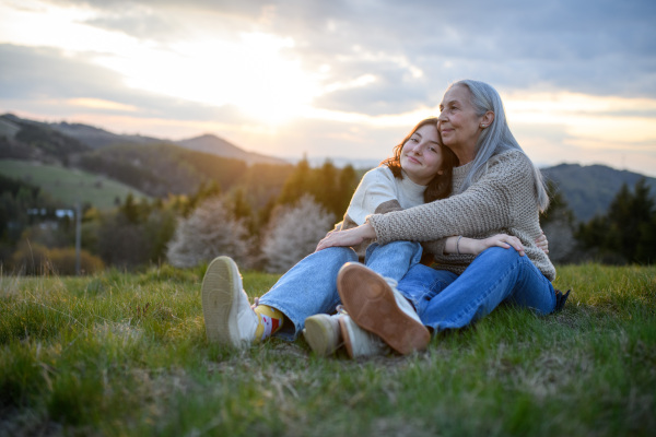 A happy senior grandmother with teenage granddaguhter hugging in nature on spring day.