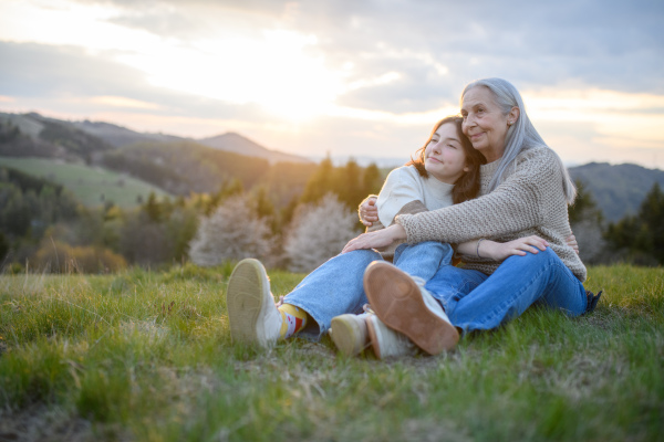 A happy senior grandmother with teenage granddaguhter hugging in nature on spring day.