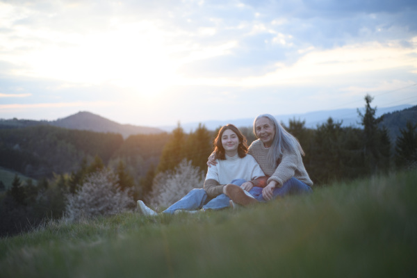 A happy senior grandmother with teenage granddaguhter hugging in nature on spring day.