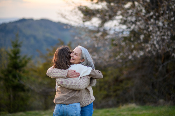 A happy senior grandmother with teenage granddaguhter hugging in nature on spring day.