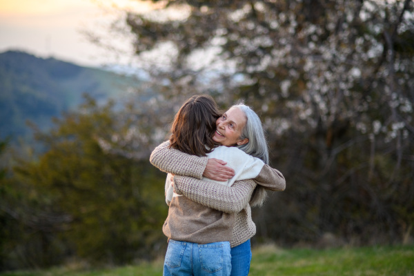 A happy senior grandmother with teenage granddaguhter hugging in nature on spring day.