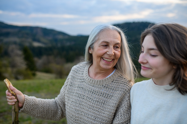 A happy senior grandmother with teenage granddaguhter on walk in nature on spring day.