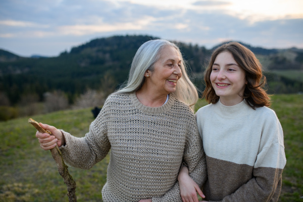 A happy senior grandmother with teenage granddaguhter on walk in nature on spring day.