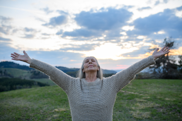 A senior woman with arms outstretched and face up at park on spring day