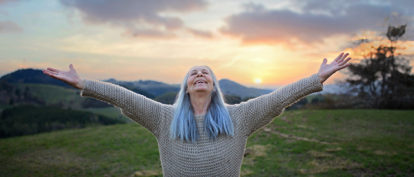 A senior woman with arms outstretched and face up at park on spring day