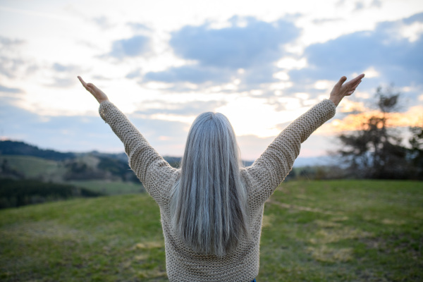 A rear view of senior woman with arms outstretched and face up at park on spring day