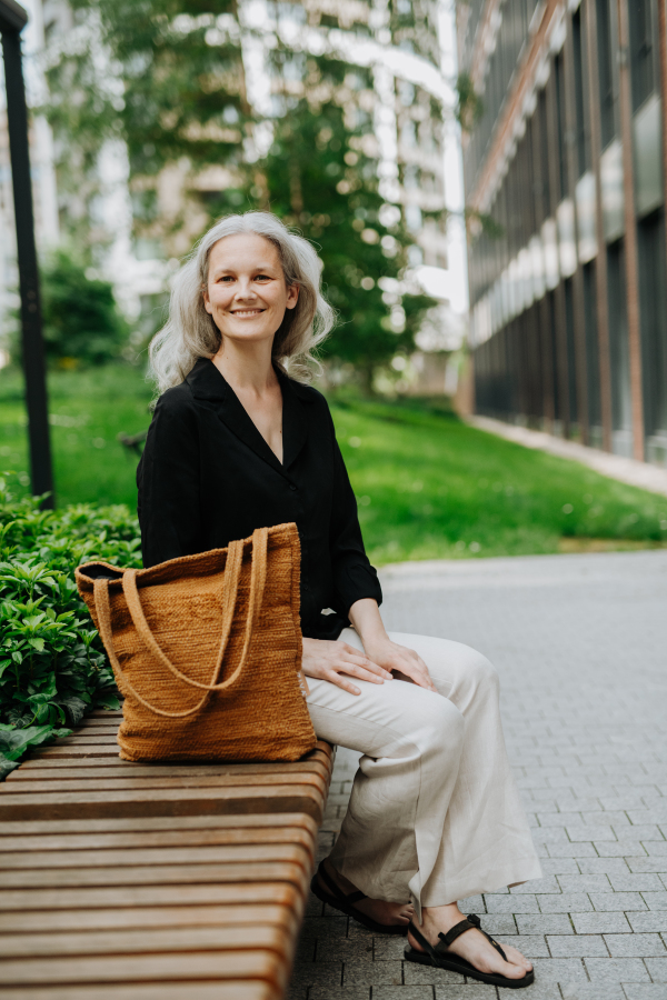 Portrait of beautiful mature woman in middle age with long gray hair, sitting on the bench in the city.