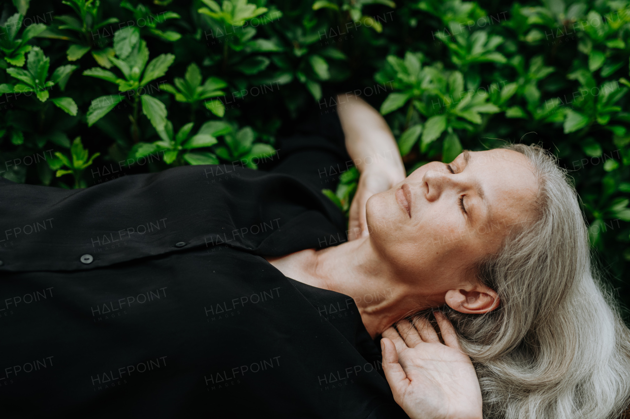 Shot from above, a beautiful mature woman in middle age with long gray hair, lying on her back with hands behind head and closed eyes.