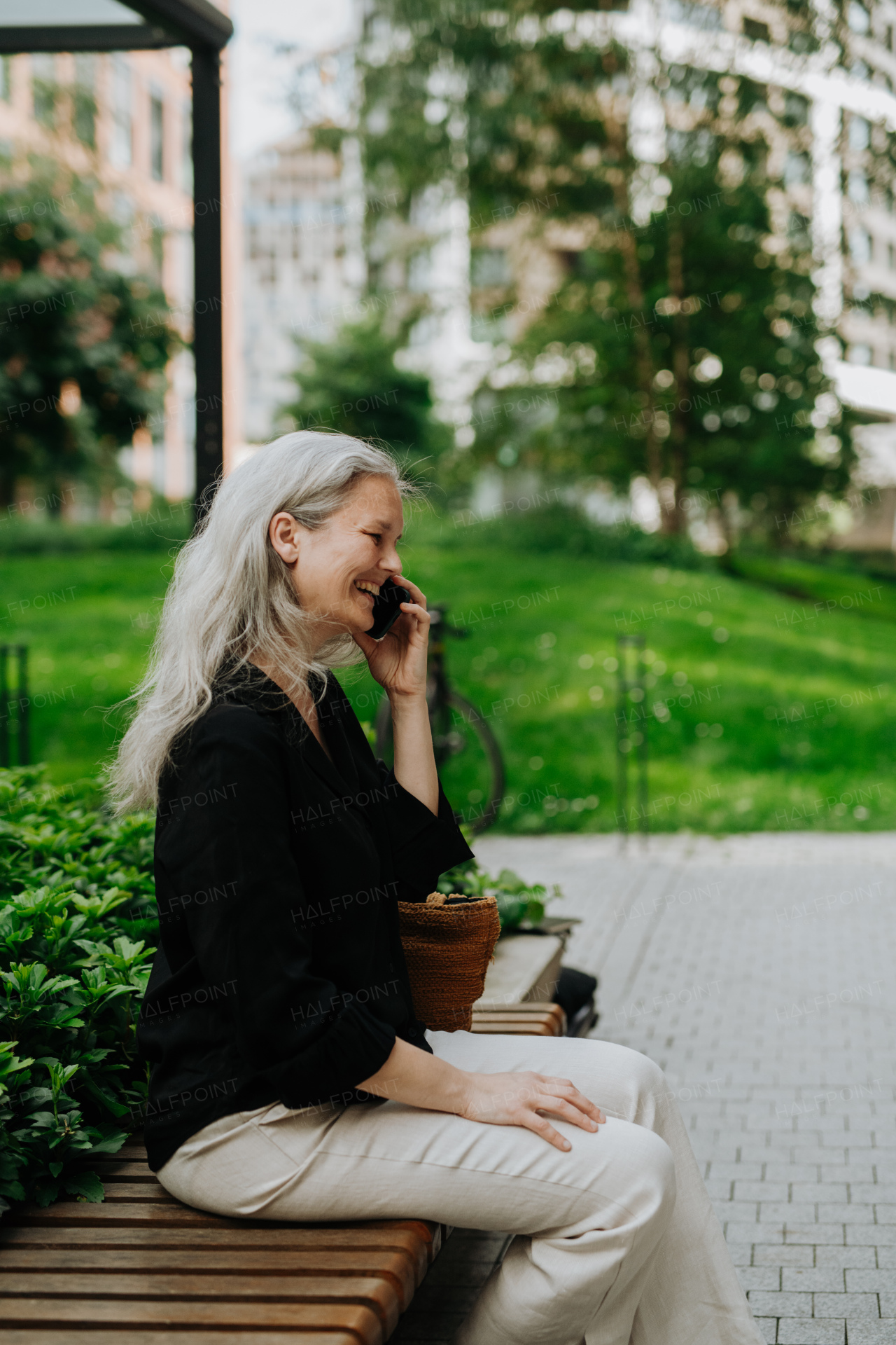 Portrait of beautiful mature woman in middle age with long gray hair, making a call outdoors in the city park.