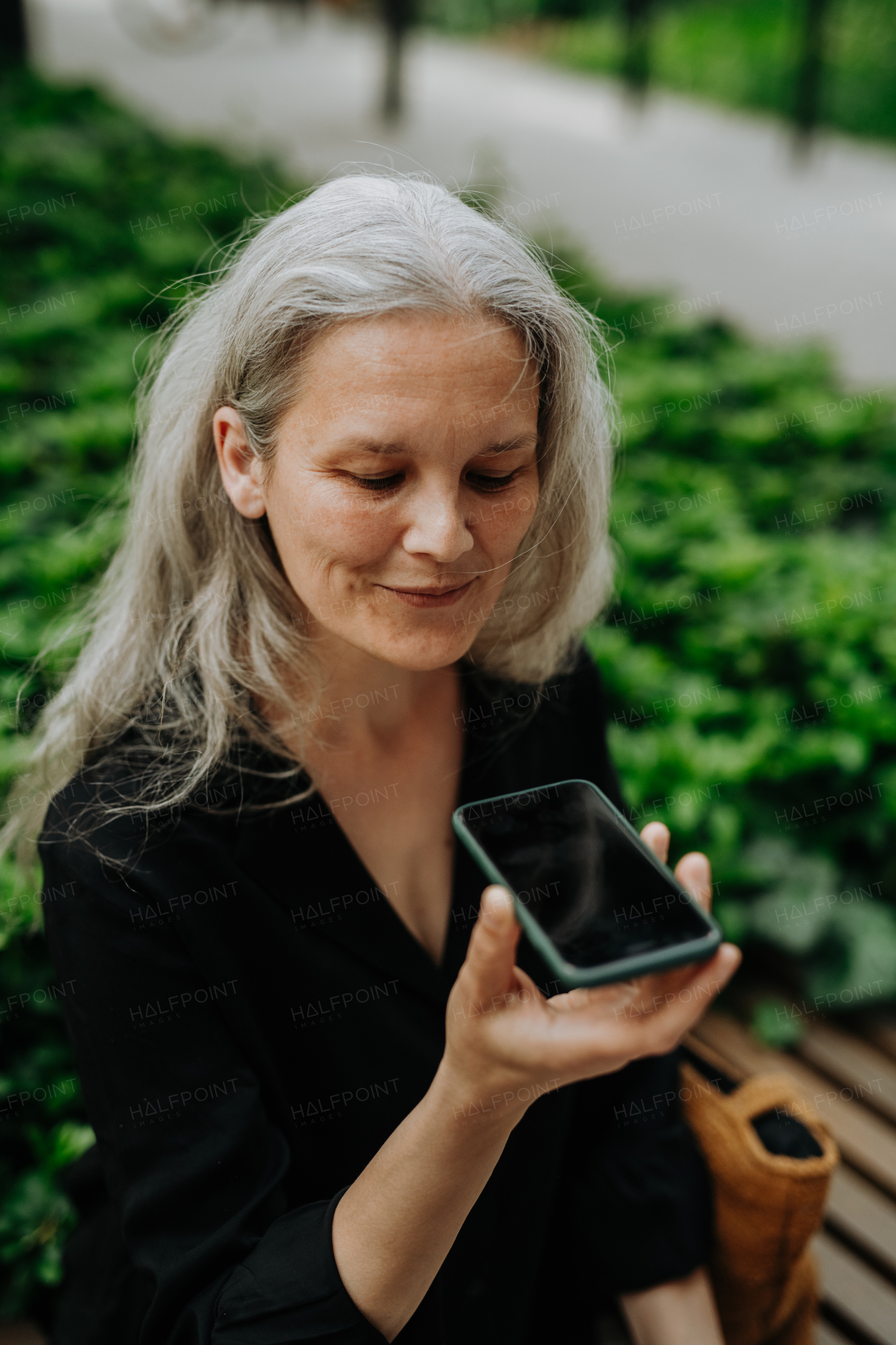 Portrait of beautiful mature woman in middle age with long gray hair, using speakerphone to make a call.