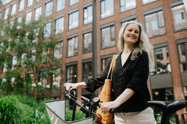 A beautiful middle-aged woman, who commutes through the city by bike, standing next to a bike rack and her bicycle. Female city commuter traveling from work by bike after a long workday.