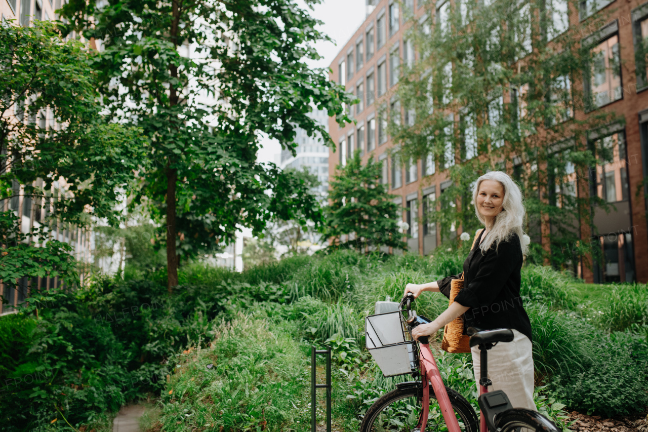 A beautiful middle-aged woman, who commutes through the city by bike, standing next to a bike rack and her bicycle. Female city commuter traveling from work by bike after a long workday.