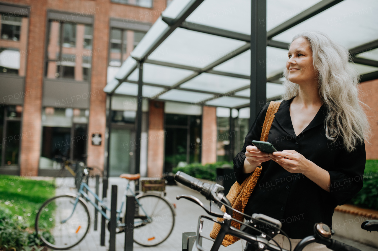 A beautiful middle-aged woman, who commutes through the city by bike, standing next to a bike rack and her bicycle. Female city commuter traveling from work by bike after a long workday.