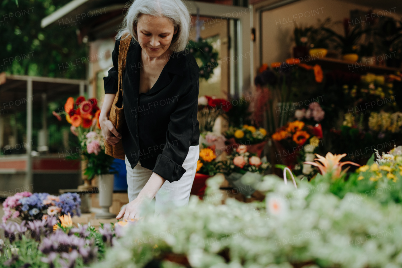 Portrait of a beautiful mature woman shopping at floral market in the city. Middle-aged woman buying fresh flowers, bouquet from market stall.