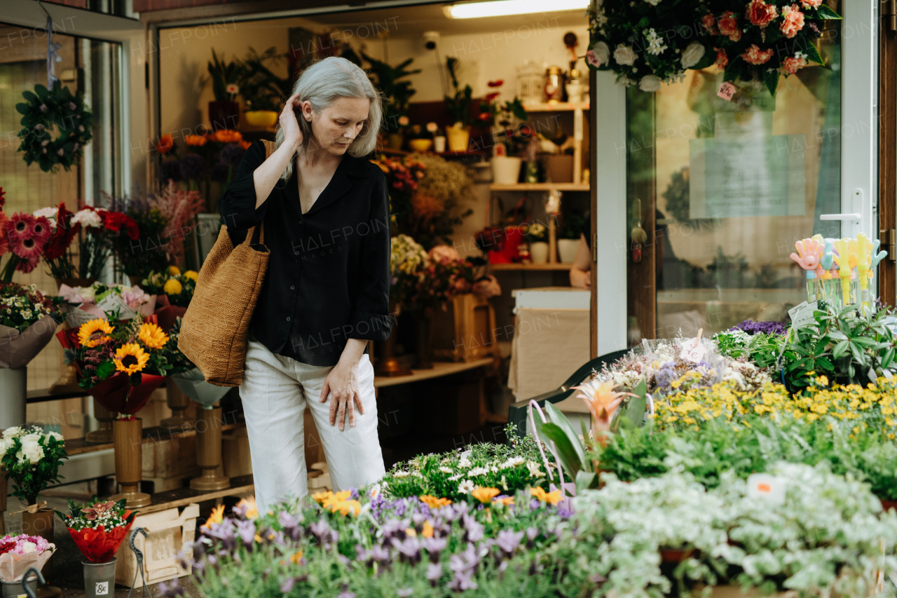 Portrait of a beautiful mature woman shopping at floral market in the city. Middle-aged woman buying fresh flowers, bouquet from market stall.