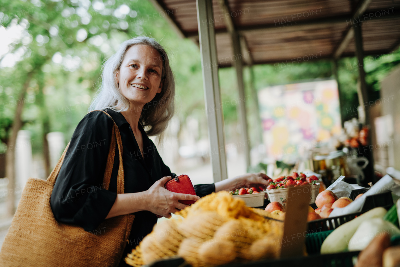 Portrait of a beautiful mature woman shopping at market in the city. Middle-aged woman buying fresh vegetables and fruits from market stall.