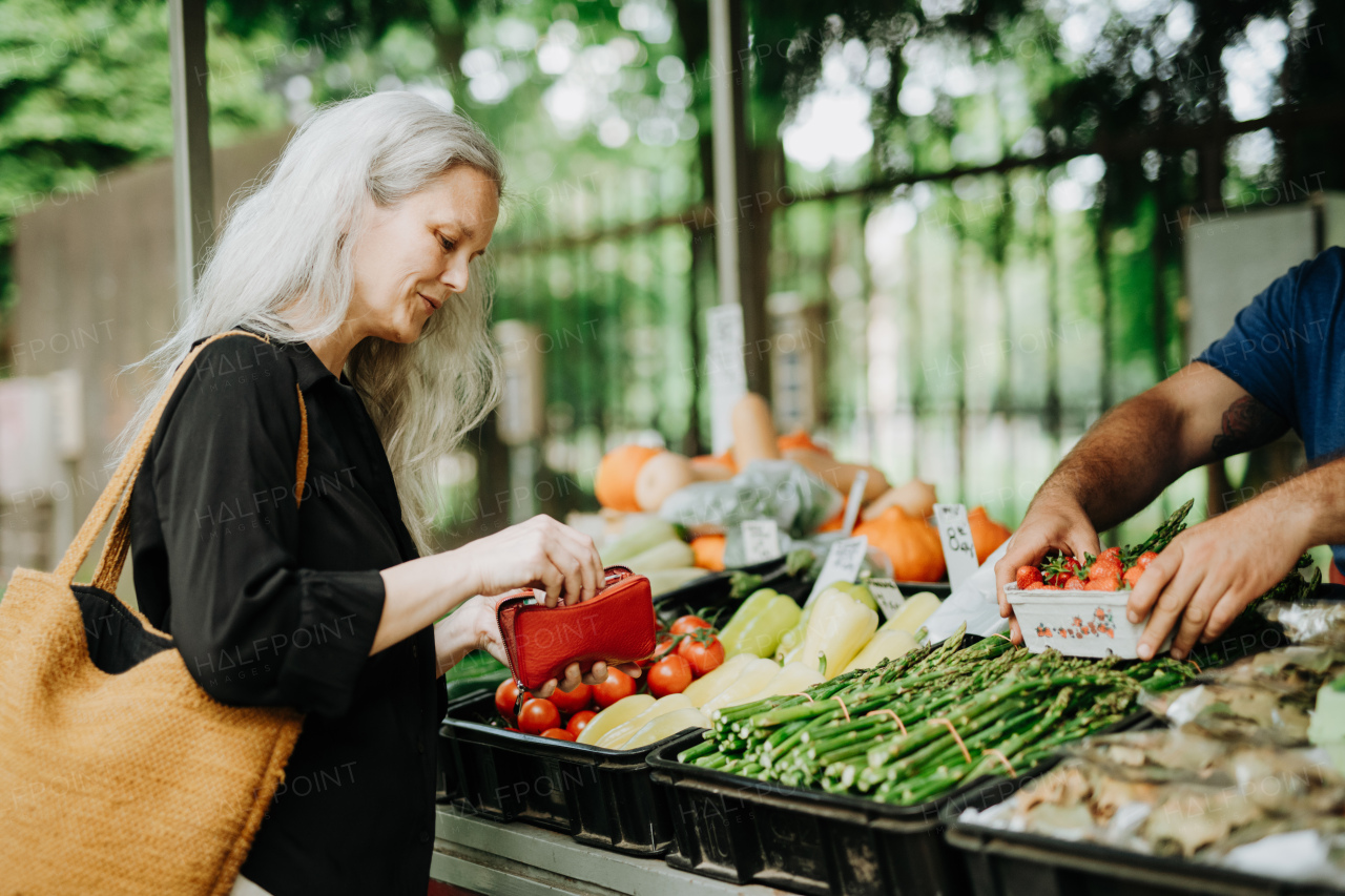 Portrait of a beautiful mature woman shopping at market in the city. Middle-aged woman buying fresh vegetables and fruits from market stall.