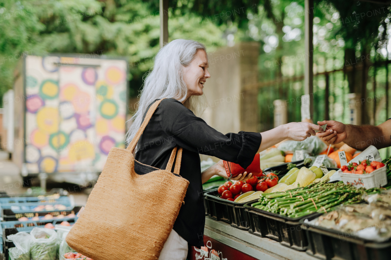 Portrait of a beautiful mature woman shopping at market in the city. Middle-aged woman buying fresh vegetables and fruits from market stall.