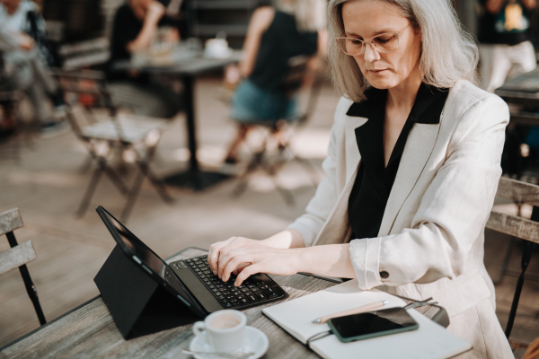 Portrait of a beautiful mature female manager with long gray hair, working outdoors in the city. The mature businesswoman using her tablet as computer. Connecting the keyboard to the tablet,