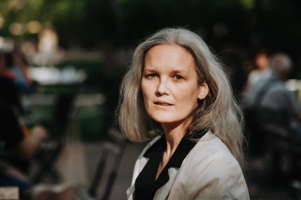 Portrait of beautiful mature woman in middle age with long gray hair, smiling and standing outdoor in the city.