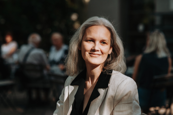 Portrait of beautiful mature female manager in middle age with long gray hair, standing outdoor in the city.