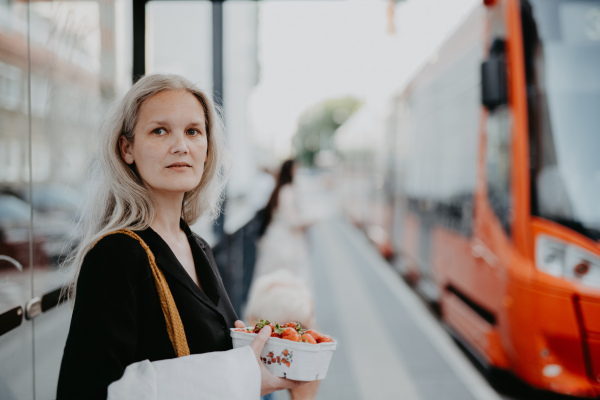 Portrait of a beautiful woman in middle age with gray hair, waiting for the bus at a bus stop. Female city commuter traveling from work by bus after a long workday.