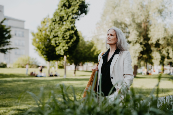 Portrait of a beautiful mature female manager with long gray hair, walking through the city. Middle-aged woman is going for walk in the city to shop.