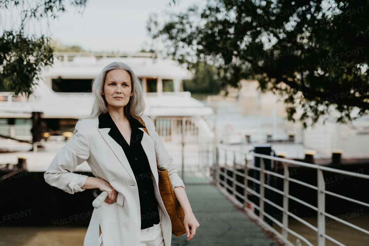 Portrait of a beautiful mature female manager with long gray hair, walking through the city. Middle-aged woman is going for walk in the city to shop.