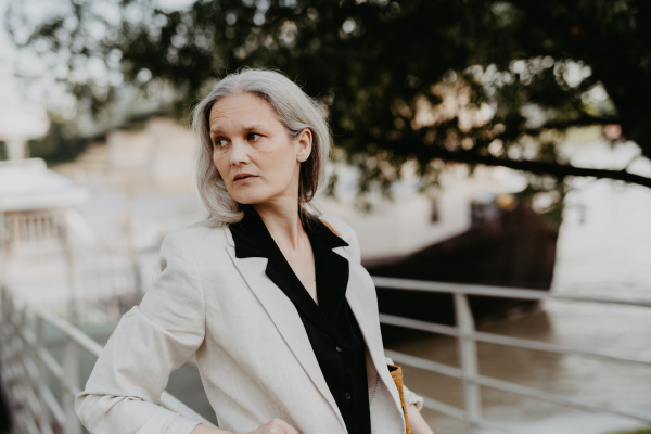 Portrait of a beautiful mature female manager with long gray hair, walking through the city. Middle-aged woman is going for walk in the city to shop.