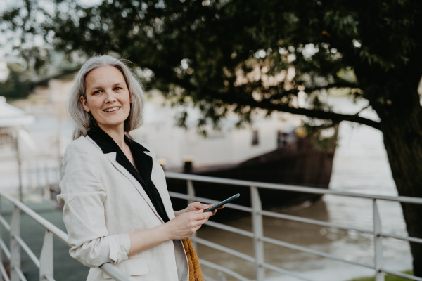 Portrait of a beautiful mature female manager with long gray hair, walking through the city. Middle-aged woman is going for walk in the city to shop.