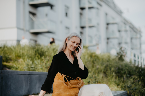 Portrait of beautiful mature woman in middle age with long gray hair, making a call outdoors in the city park.