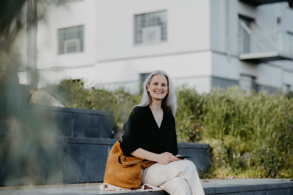 Portrait of a beautiful woman with gray hair, sitting on concrete stairs with closed eyes, enjoying warm summer weather in the city.