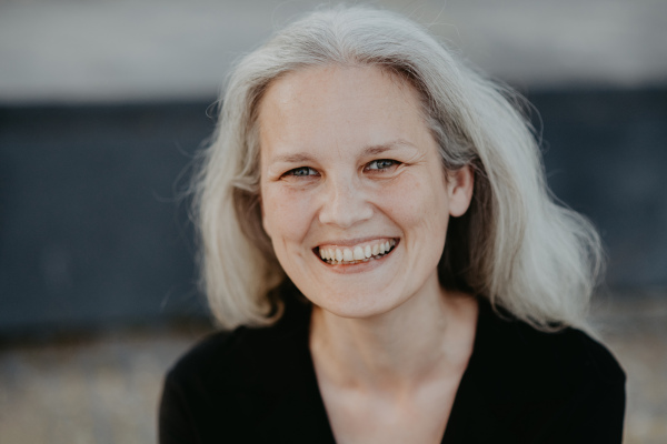 Portrait of beautiful mature woman in middle age with long gray hair, smiling and standing outdoor in the city.