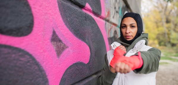 Portrait of young muslim woman with sports gloves, standing in front of a graffiti.