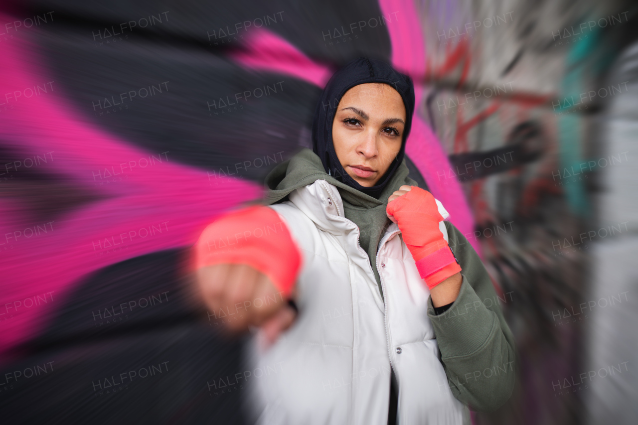 Portrait of young muslim woman with sports gloves, standing in front of a graffiti.