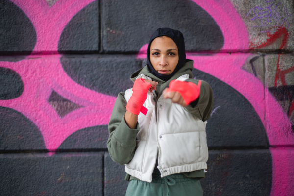 Portrait of young muslim woman with sports gloves, standing in front of a graffiti.