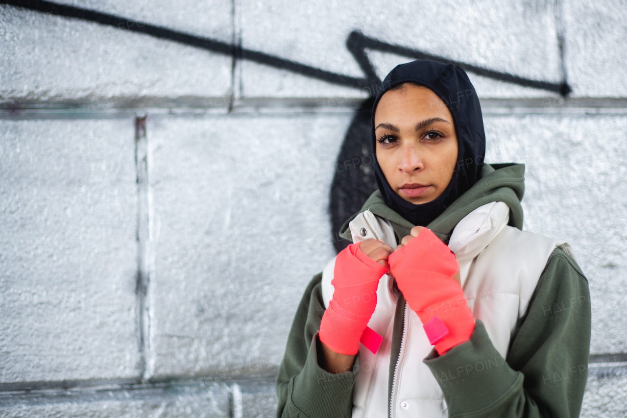 Portrait of young muslim woman with sports gloves, standing in front of a graffiti.