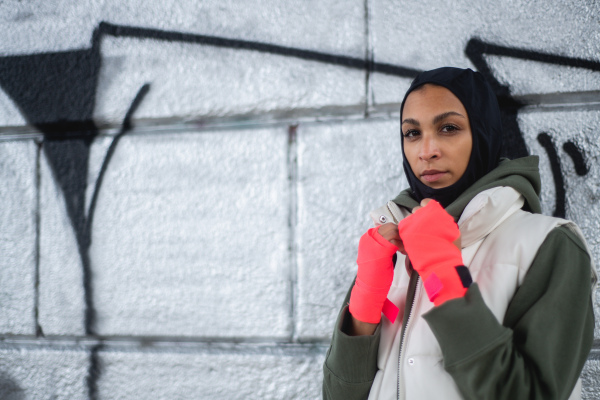 Portrait of young muslim woman with sports gloves, standing in front of a graffiti.