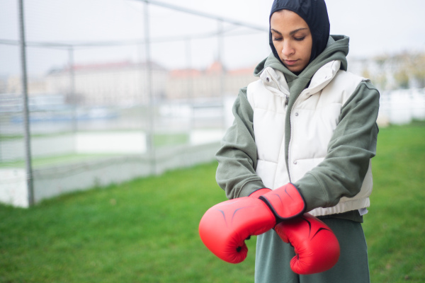 Unhappy muslim woman with the boxing gloves standing outdoor.