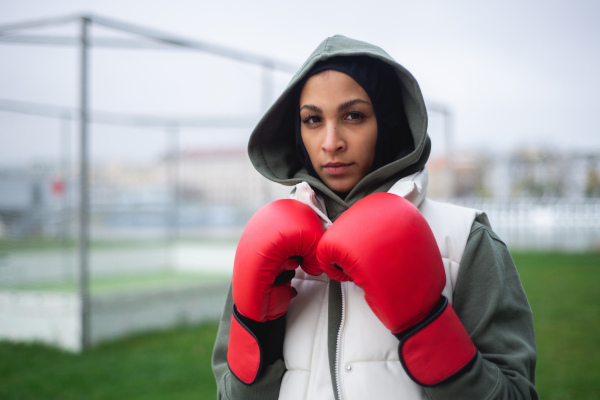 Portrait of a young muslim woman with boxing gloves standing outdoor.