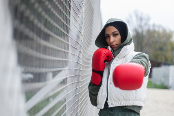 Portrait of a young muslim woman with boxing gloves standing outdoor in a city.