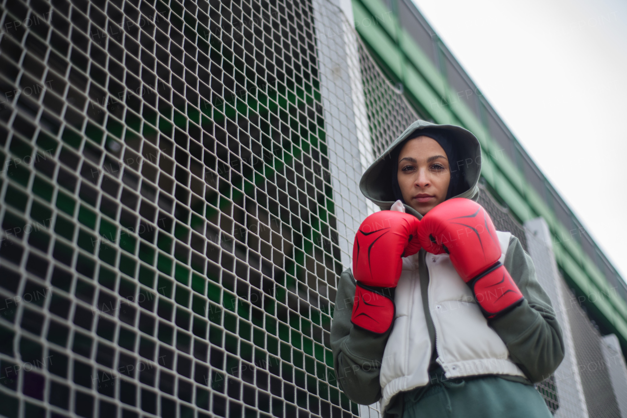 Portrait of a young muslim woman with boxing gloves standing outdoor.