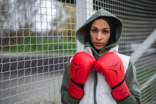 Portrait of a young muslim woman with boxing gloves standing outdoor.