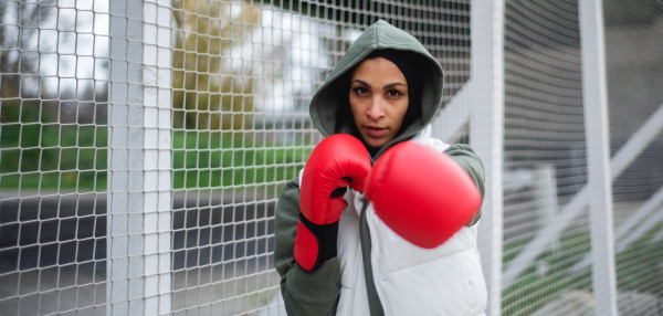 Portrait of a young muslim woman with boxing gloves standing outdoor in a city.