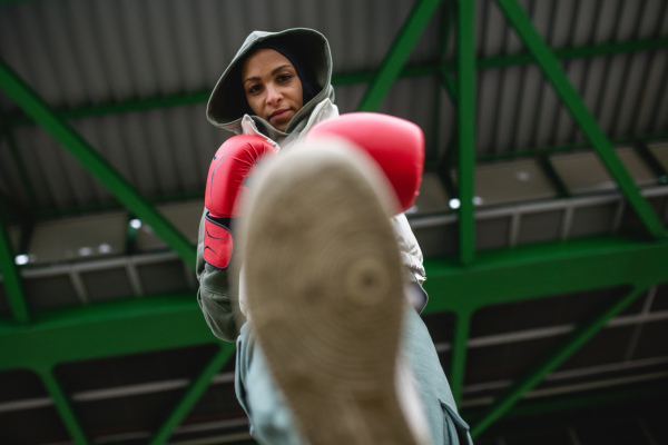 Low angle view of a young muslim woman with boxing gloves standing outdoor in a city.