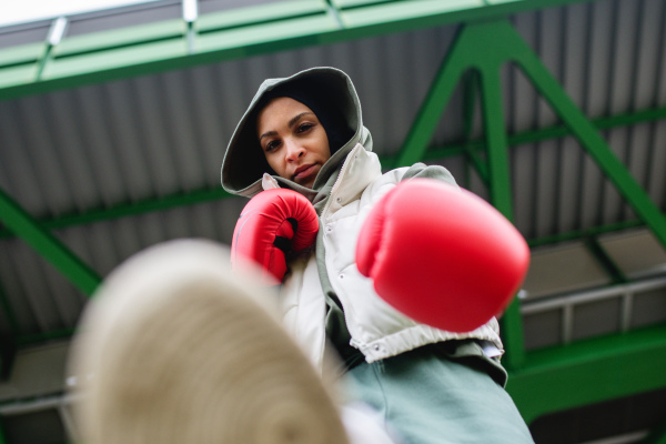 Low angle view of a young muslim woman with boxing gloves standing outdoor in a city.